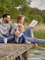 VRK Risiko-Lebensversicherung – Eine junge Familie sitzt zusammen auf einem Steg am See.